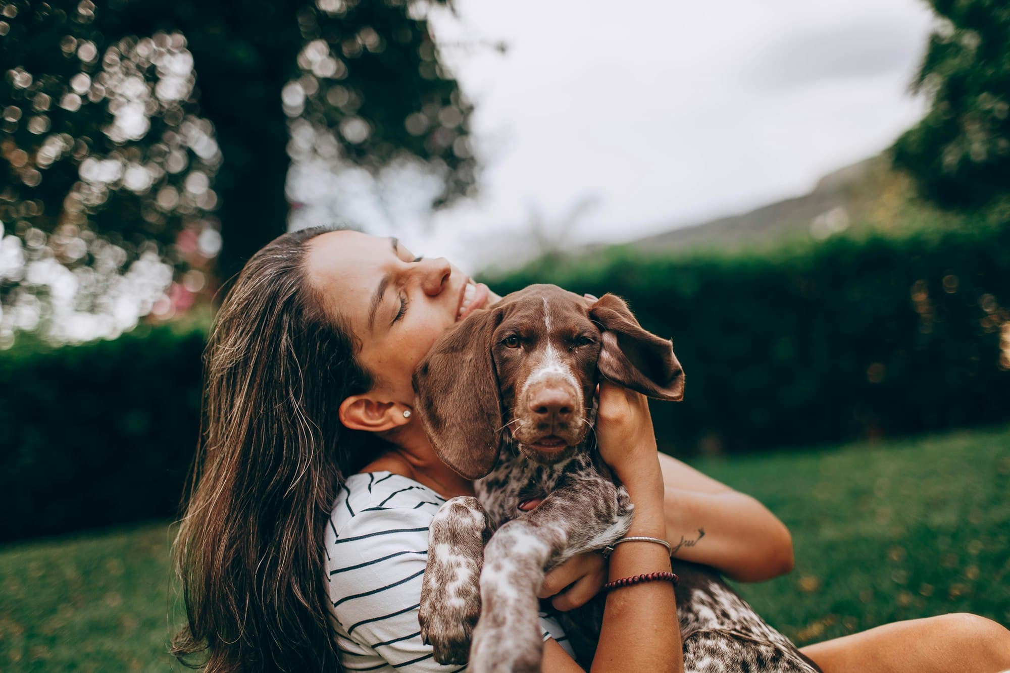 A woman gently hugging a brown and white spotted puppy outdoors in a garden